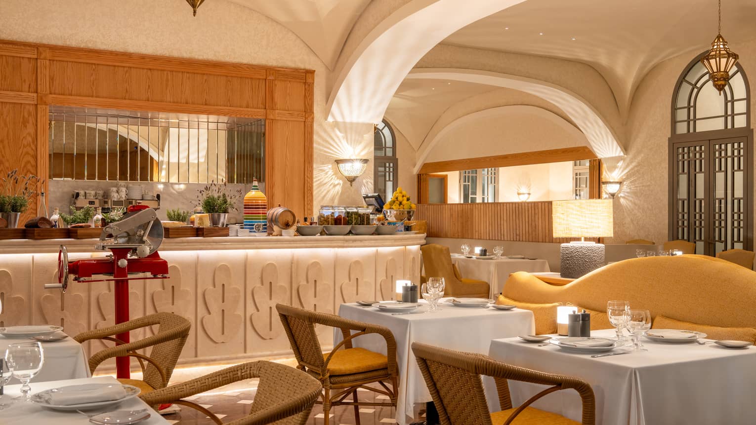 Indoor restaurant with buffet counter and white-tablecloth tables, wicker chairs and yellow sofas