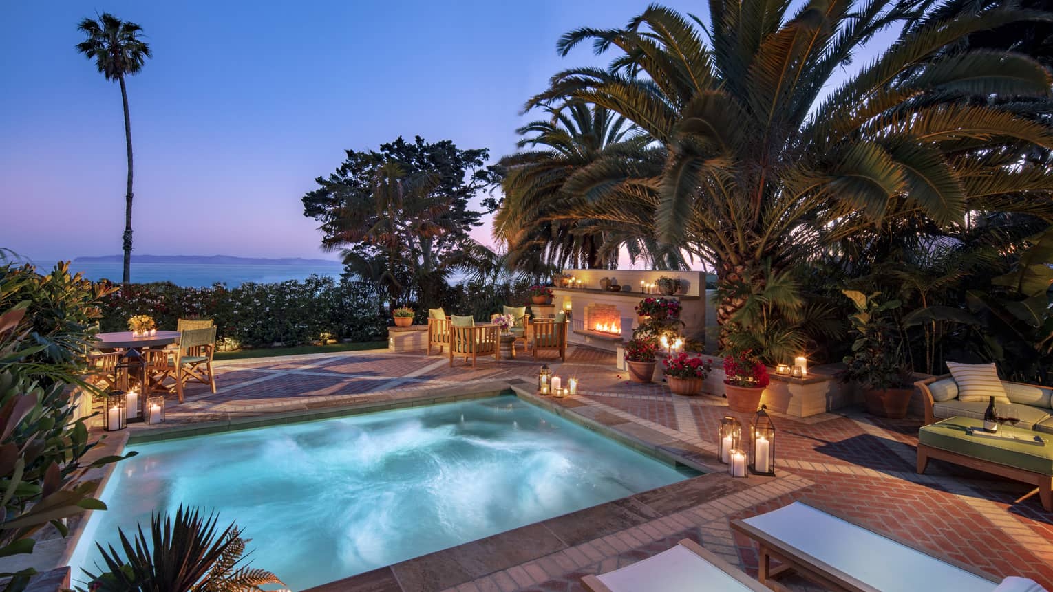 Illuminated villa plunge pool and patio, palm trees at dusk