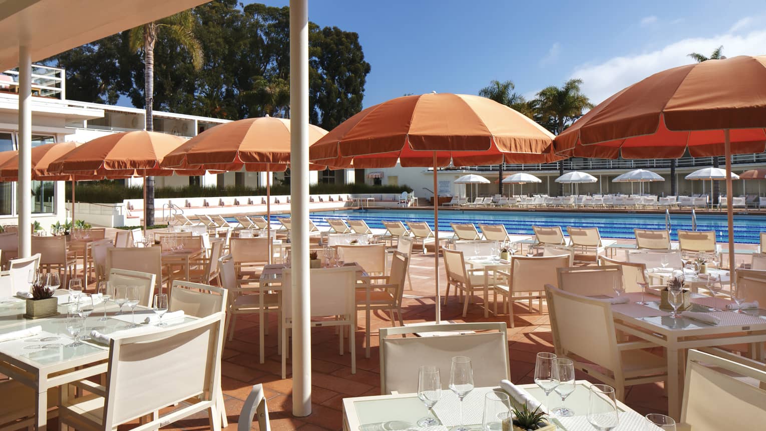 Coral Cafe and Bar patio, orange umbrellas over white dining tables, chairs by pool