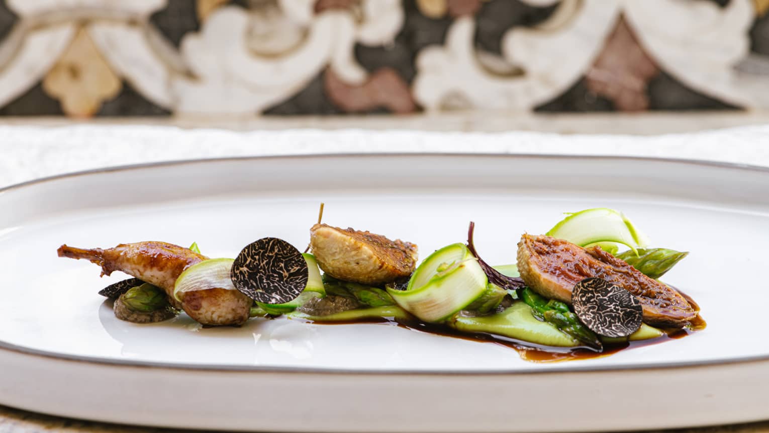 Quail pieces with green asparagus shavings and sliced black truffle on oval ceramic dish