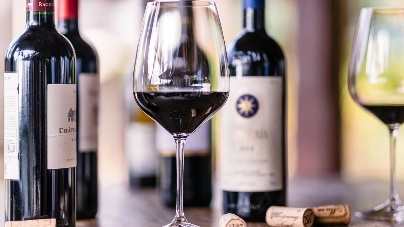 Closeup of glass of red wine, bottles beside it
