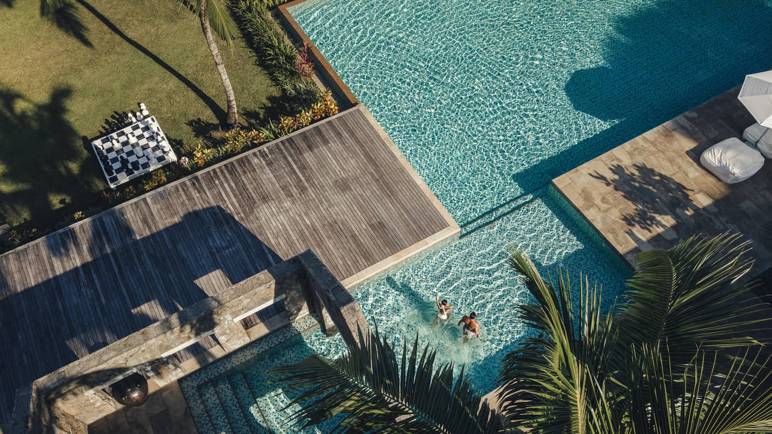 Aerial view of sparkling blue pool surrounded by decking and palm trees