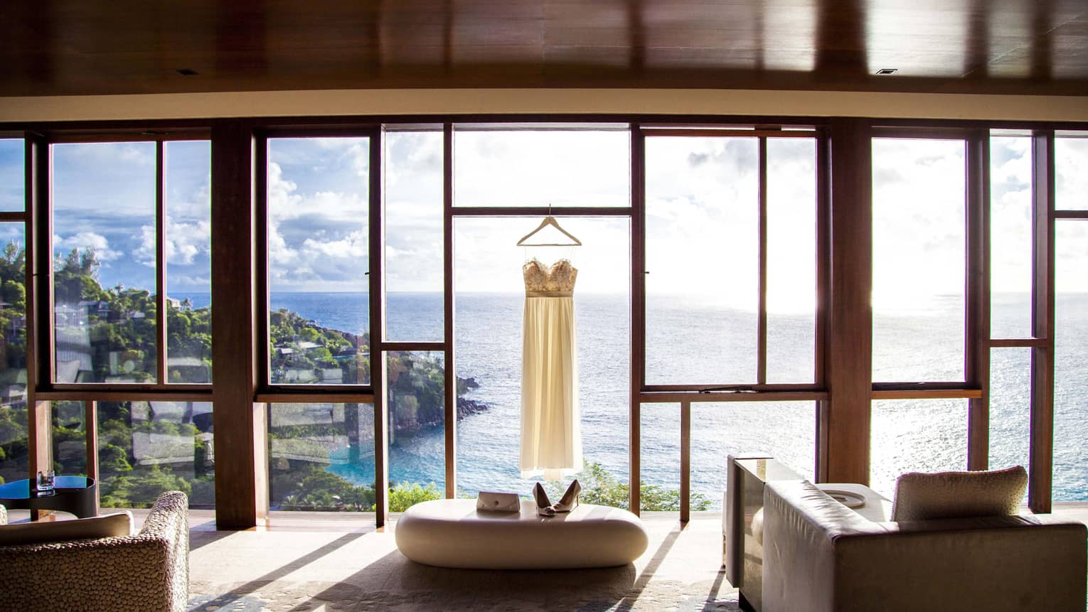 Strapless wedding gown hangs in front of floor-to-ceiling windows overlooking Petit Anse Bay