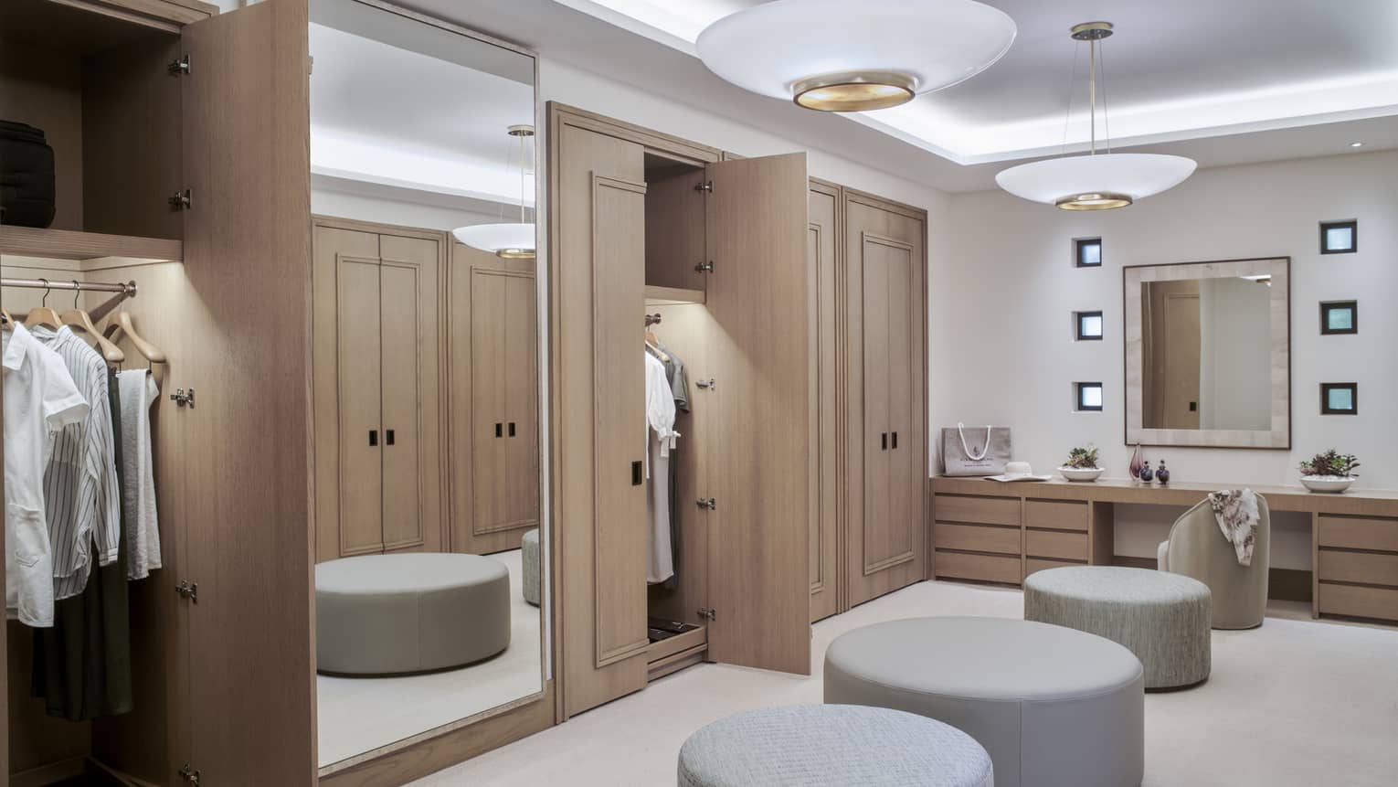 Large dressing room with four circular benches, wall of closets and mirrors, vanity