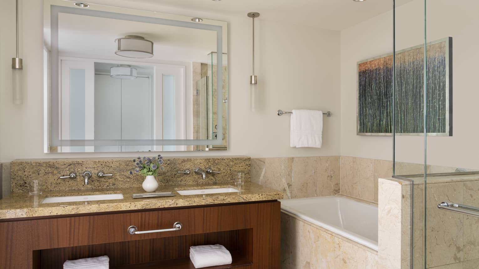 Luxury bathroom with a granite double vanity, mirror, bathtub surrounded by beige tile, wall art, and a glass-enclosed shower