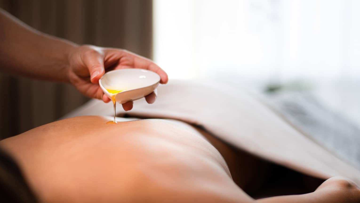 A spa staff member pouring liquid onto a woman?s back.