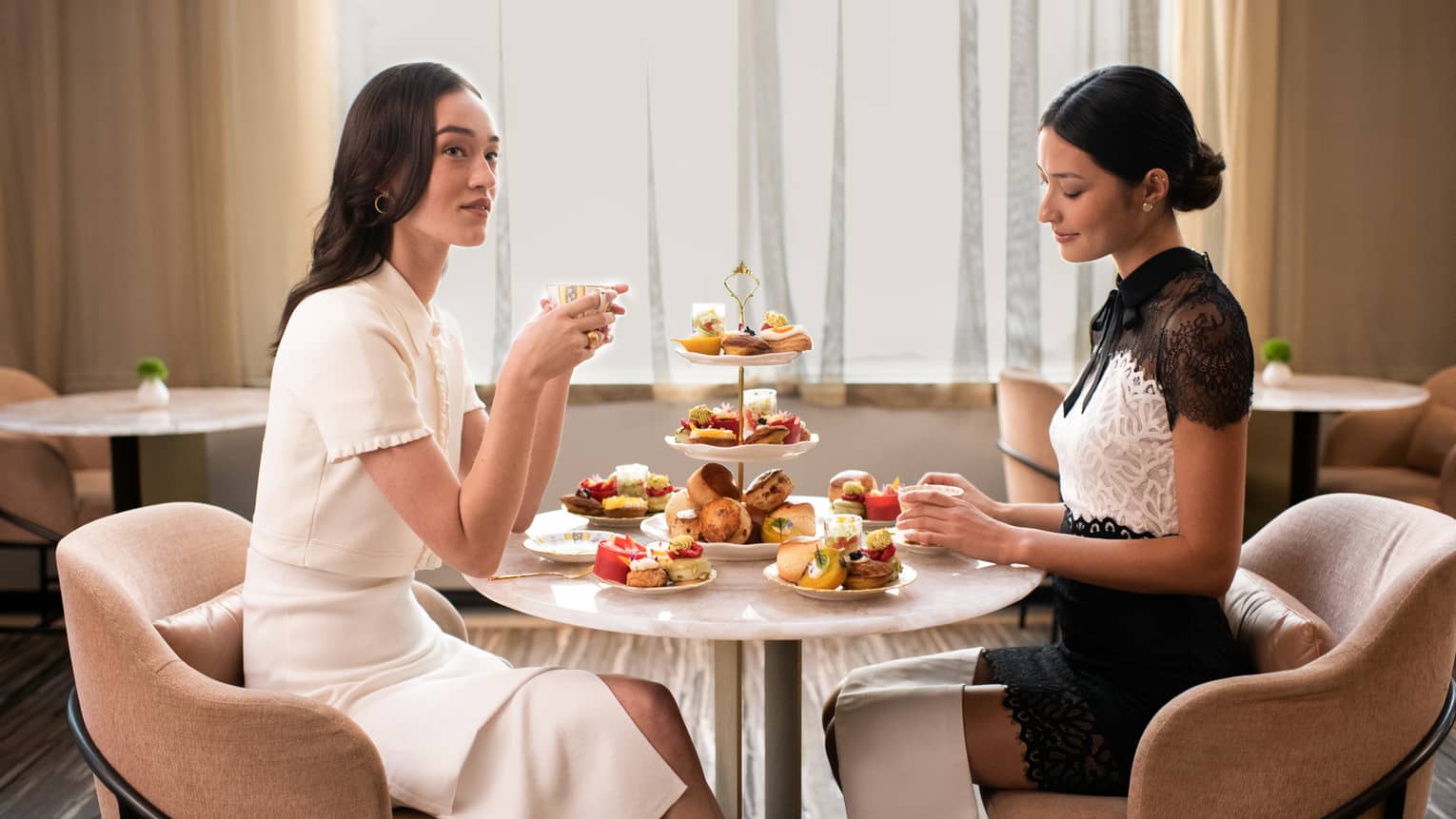 Two guests enjoy a formal tea service including sumptuous sweets and pastries and a three-tiered stand laden with delicacies.