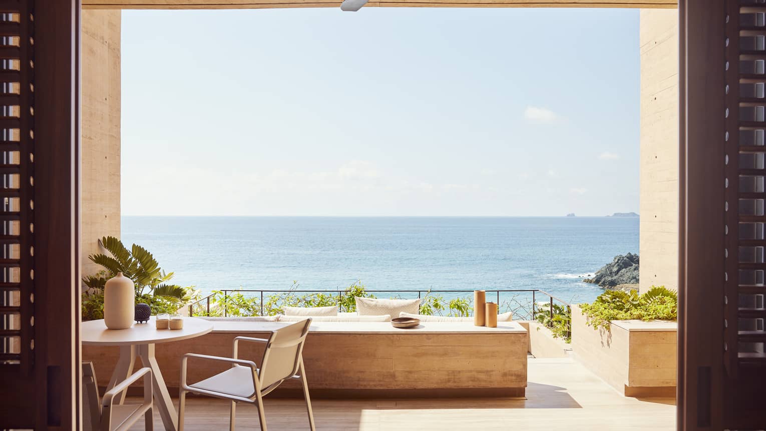 The exterior of a beachfront room with a small table and a large opening looking out at an ocean.