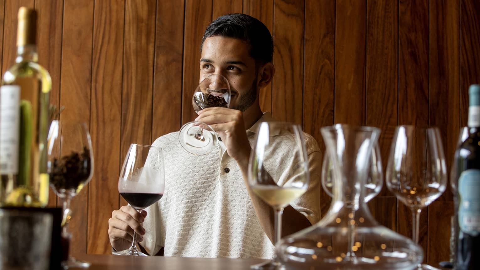 At a wine tasting, a guest smells coffee beans in a glass before tasting the glass of dark red wine held in his other hand.