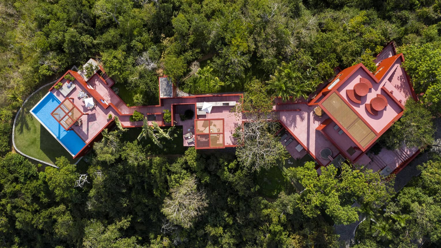 Aerial view of a villa comprised of three red buildings, nestled in the jungle