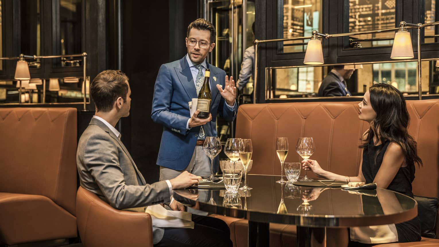 Couple with wine glasses in La Dame de Pic London booth while sommelier introduces bottle of white wine