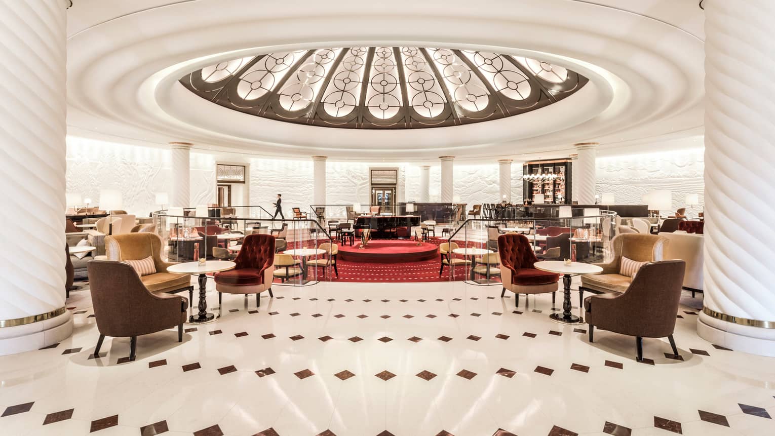 Rotunda bar cocktail tables and chairs around sunken lounge with red carpets, grand piano, dome ceiling