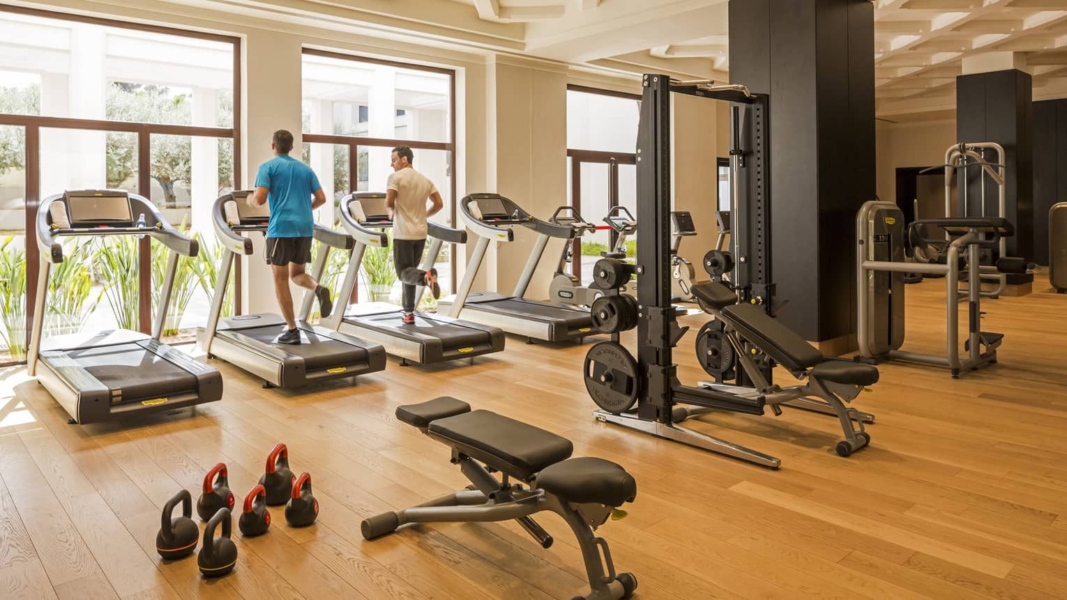 Two men workout on treadmills overlooking outdoors in gym with weight machines in foreground