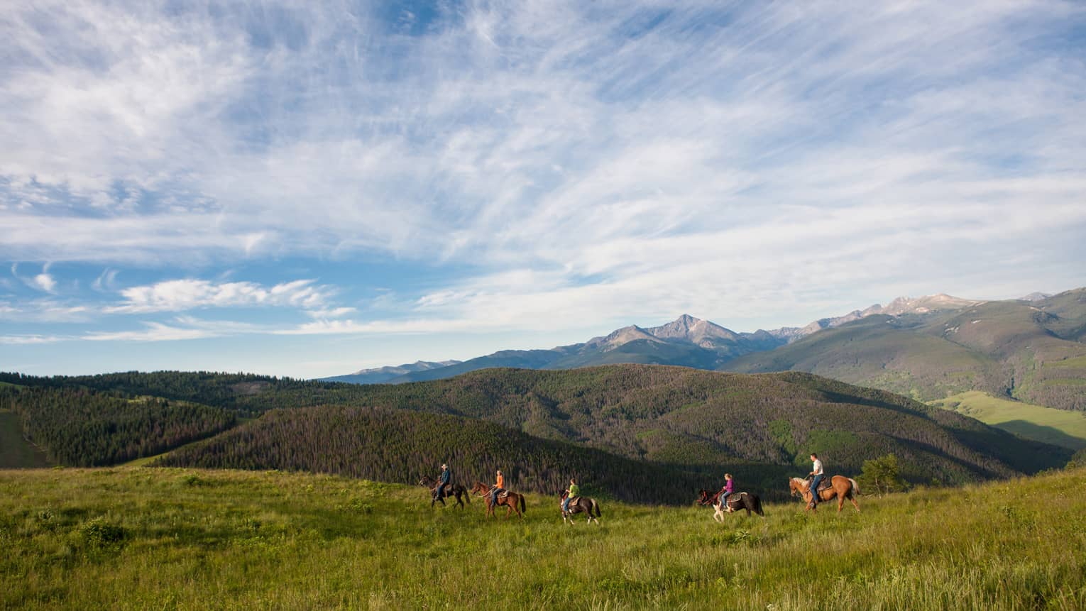 A group of people on horseback riding along grass and hills.