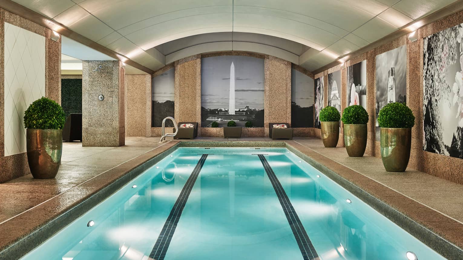 Long indoor lap swimming pool, large gold planters on deck, wall with black-and-white mural of the Washington Monument