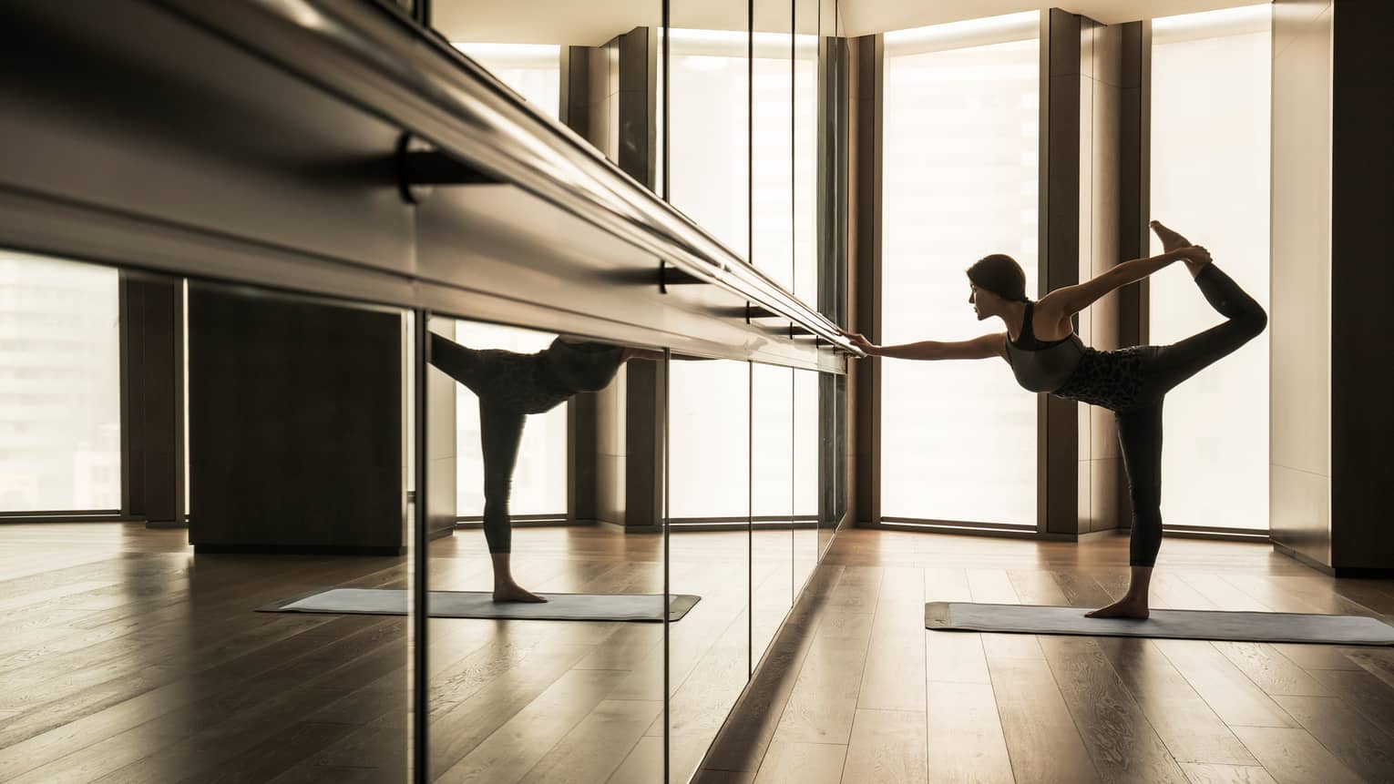 Woman stretching leg behind her while touching bar in fitness studio