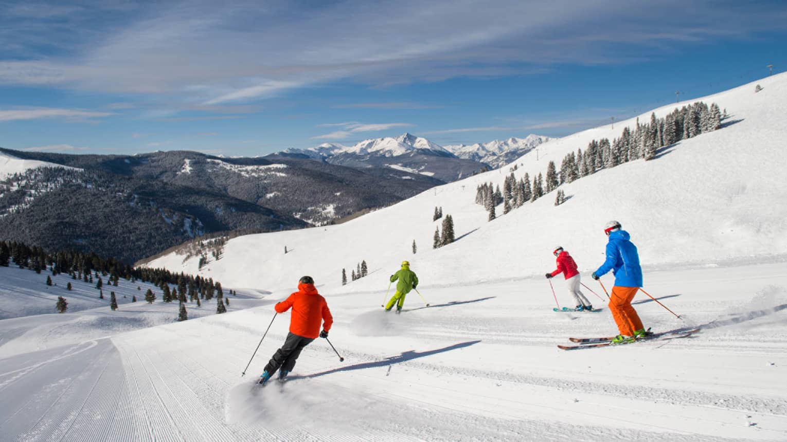Four skiers in brightly coloured coats ski down mountain covered in snow