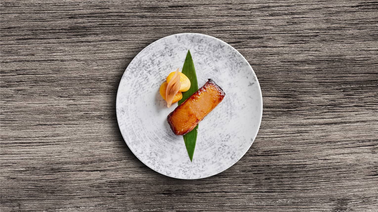 Cooked fish with miso, apricot and ginger on a grey plate.
