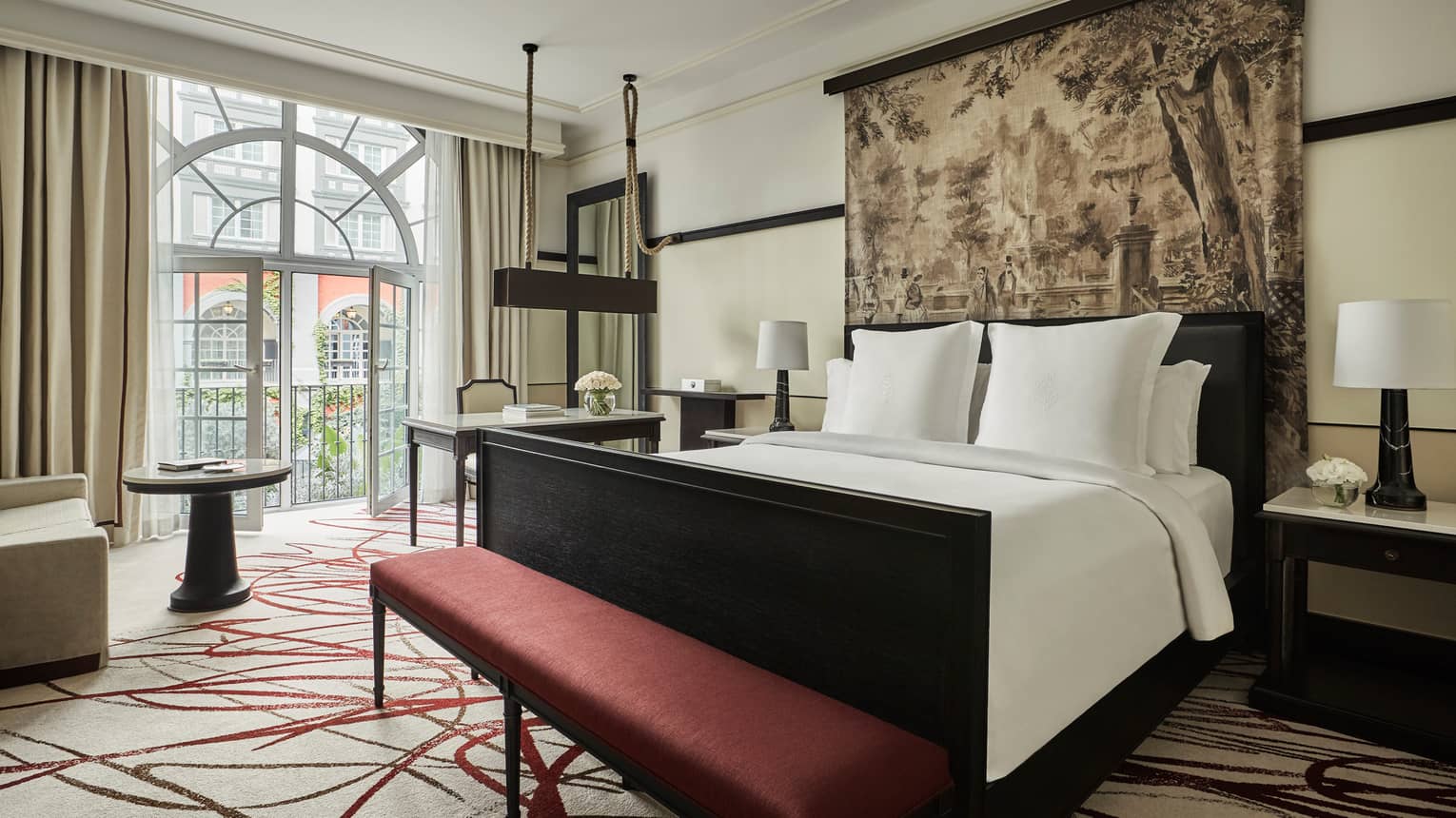 Premier Room bed under print headboard, red bench at foot, sunny arched balcony glass doors