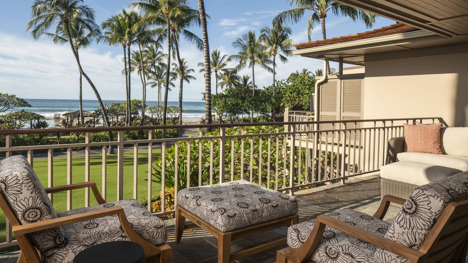 Outdoor balcony with two cushioned chairs and matching ottoman, view of lawn, palm trees and ocean
