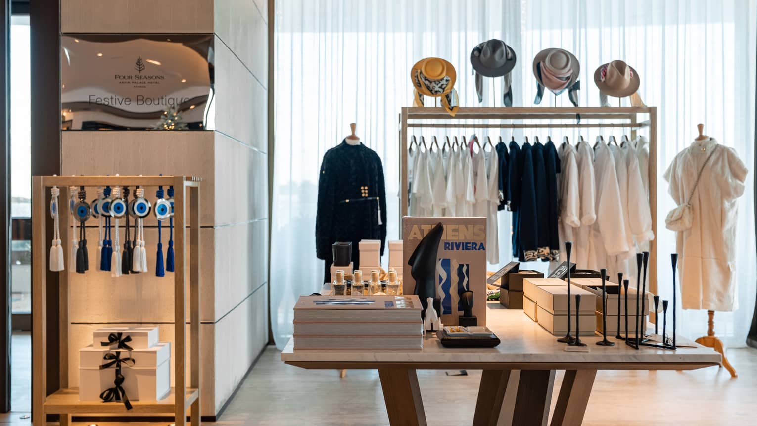 Small hotel boutique with rack of clothing topped with four hats and other displays in room