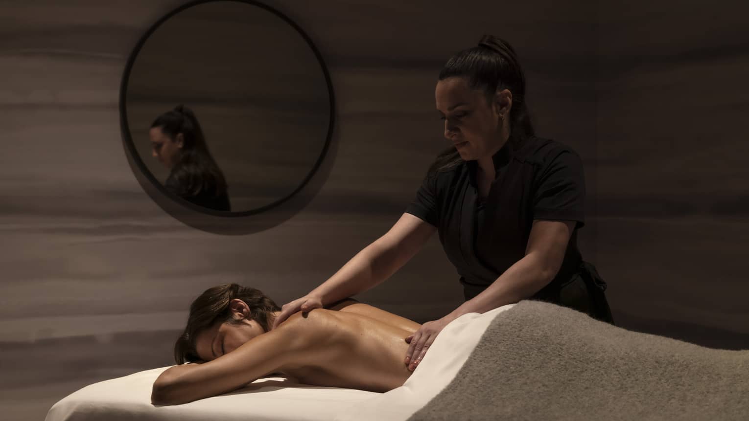 A spa staff member massaging a woman in a dimly lit room.