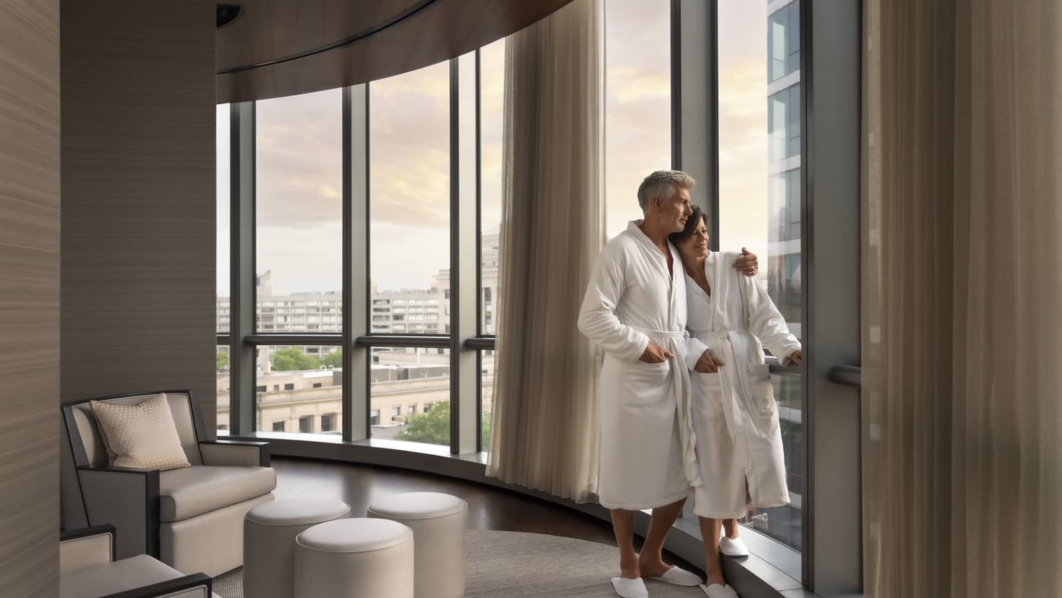 A man and woman in spa robes looking out a window.