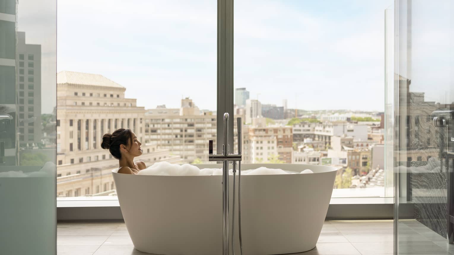 A woman in a bathtub next to a large window.