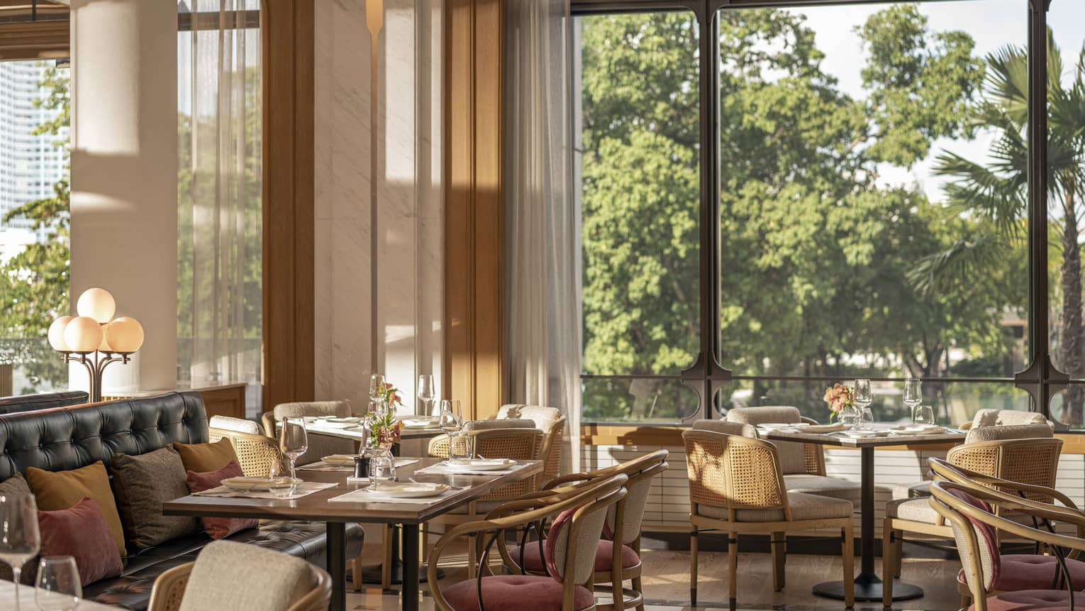 Riva restaurant with square tables set for four, comfortable chairs, floor-to-ceiling windows with natural lighting