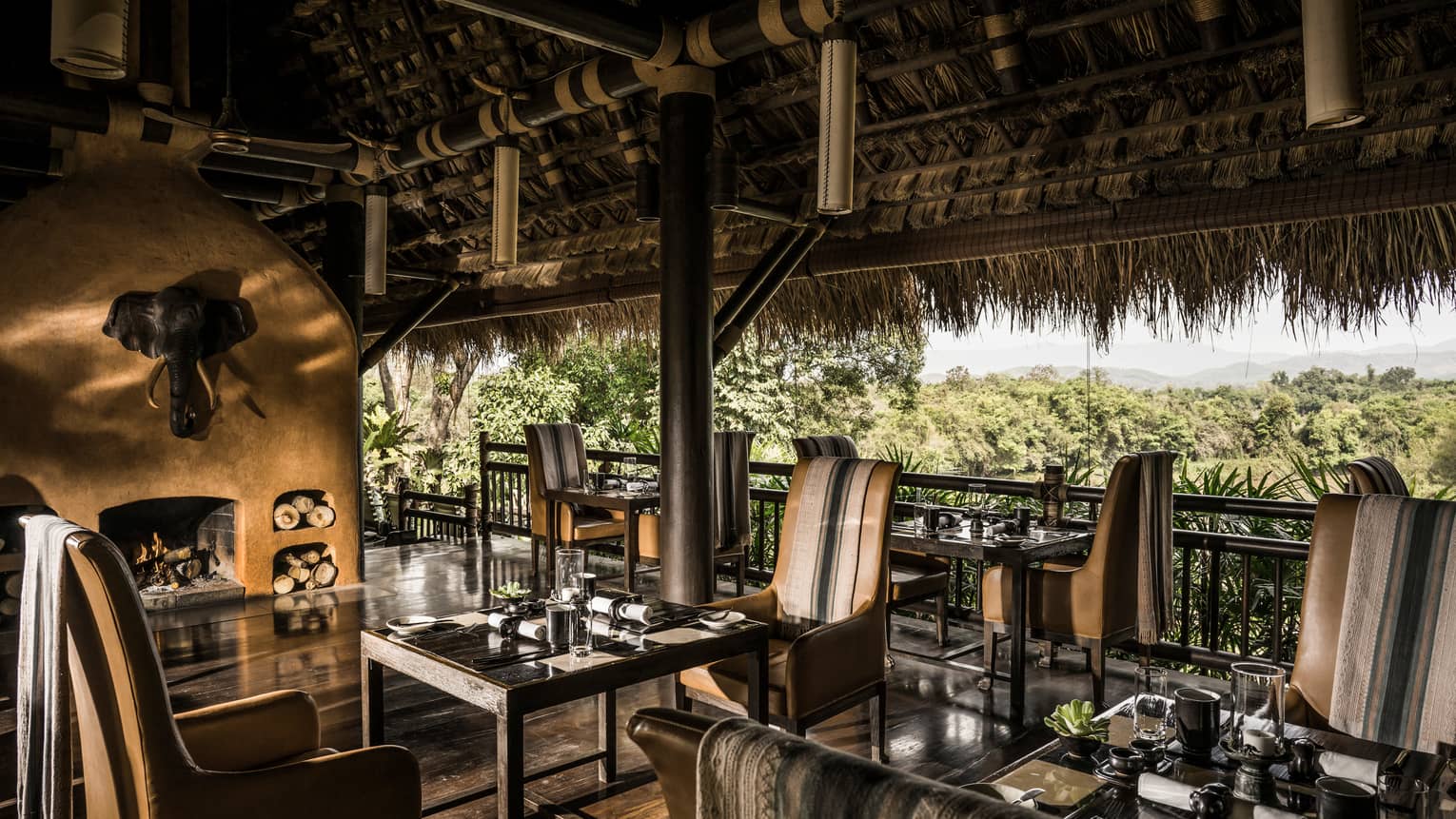 Dining tables, leather chairs in wood open-air restaurant under thatched roof 