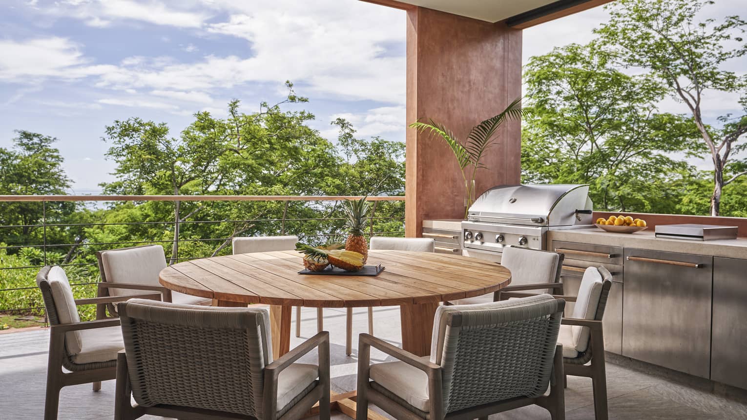 Outdoor covered patio with round wooden table and 8 chairs, set next to outdoor grill and counter