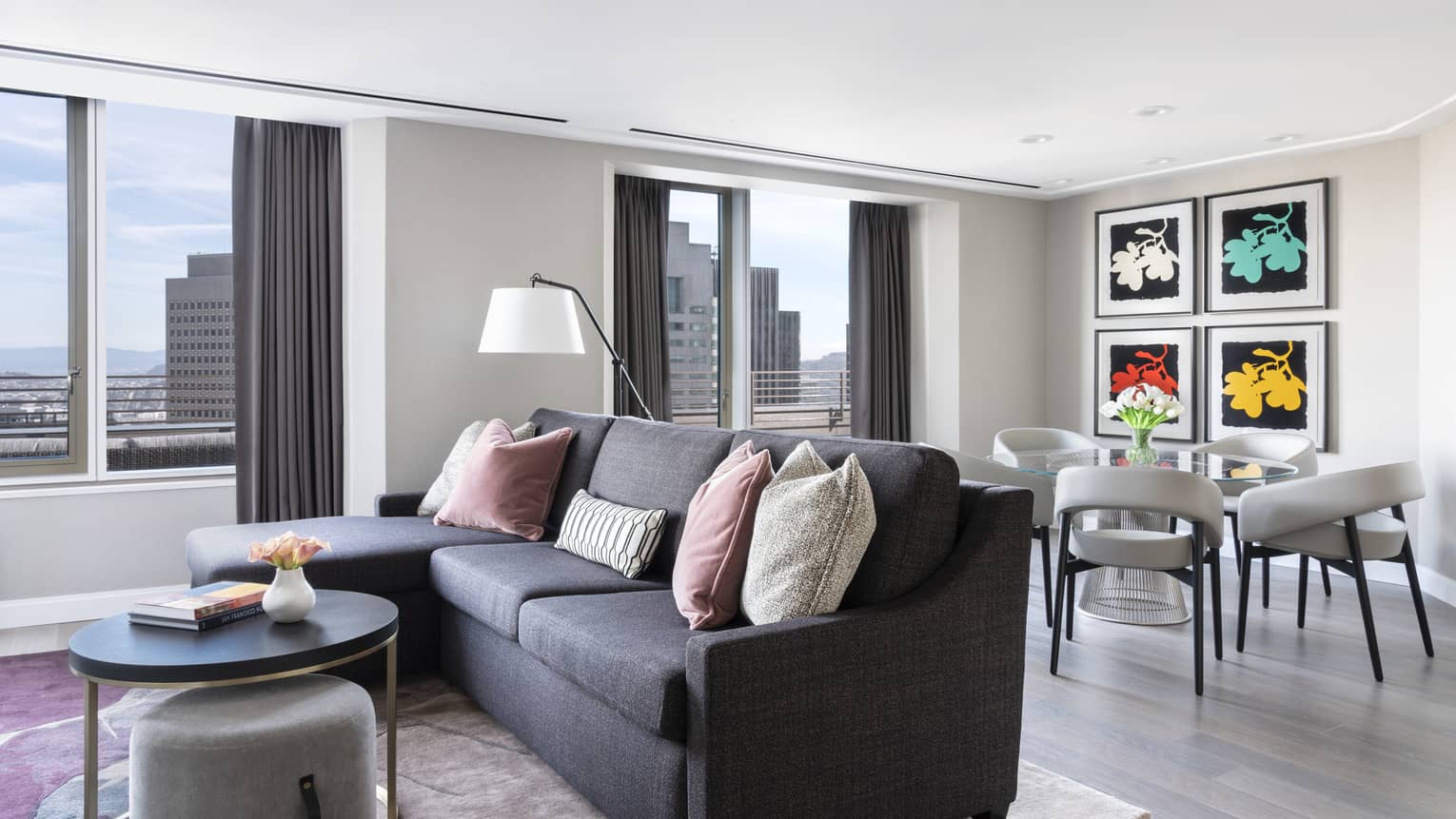 Living room with charcoal-grey sofa, dining table for four, artwork and city view