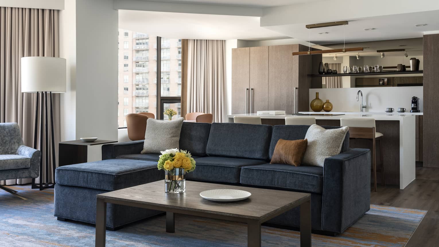 Living room with dark grey sofa, wooden coffee table, kitchen in the back