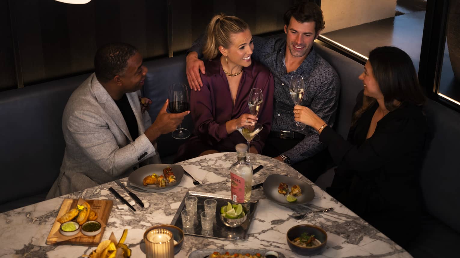 A group of people sitting at a booth in a dining outlet surrounded by food.