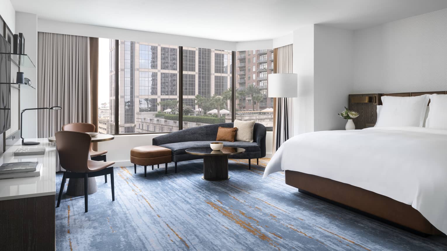 Hotel room with blue carpeting, king bed, dark blue chaise lounge, large windows