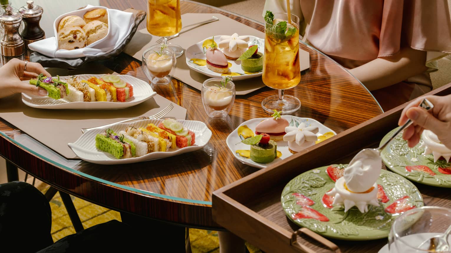 A wooden dining table scattered with afternoon tea dishes and drinks