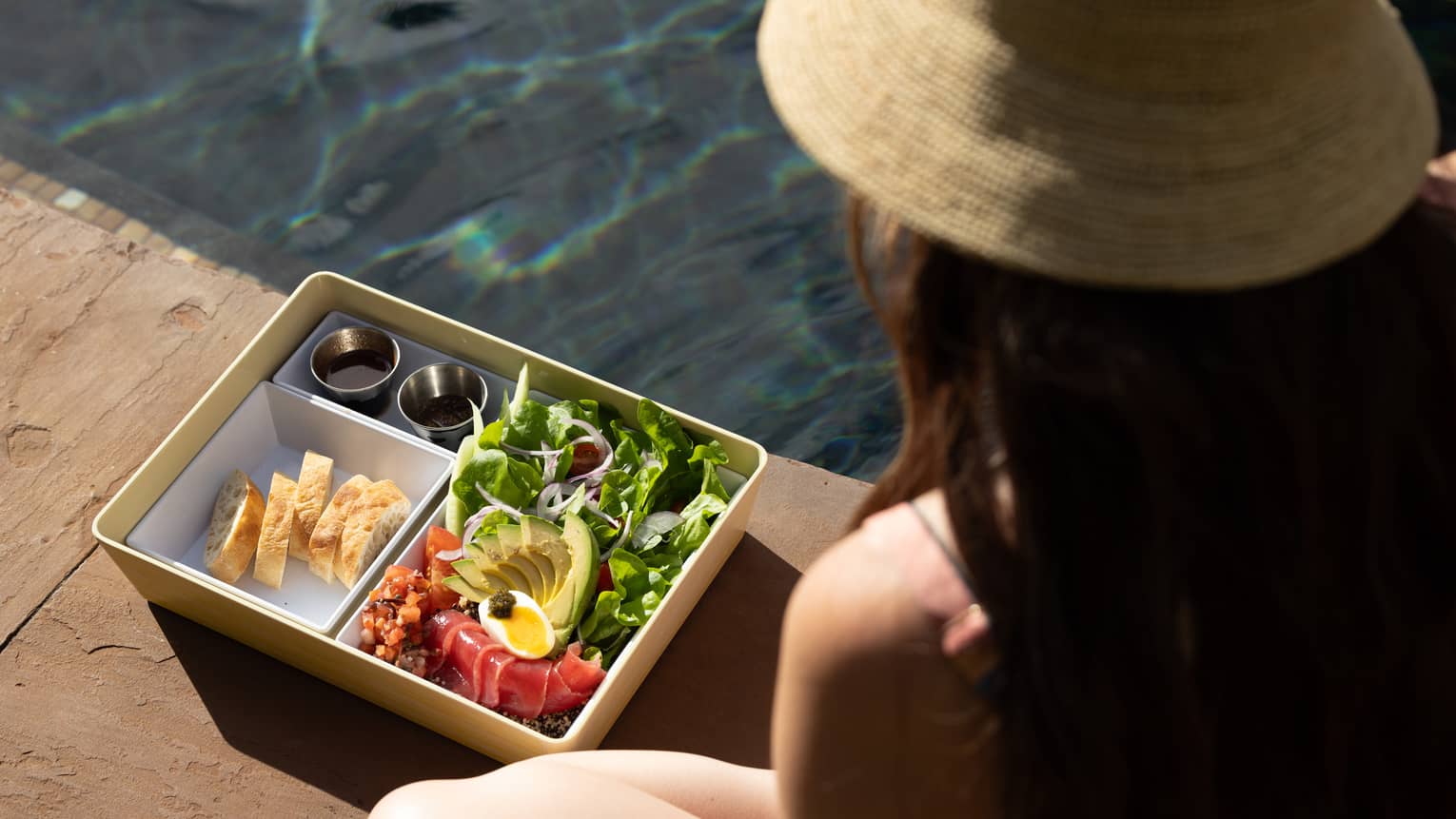 A woman sits next to the pool with a poolside, healthy bento box