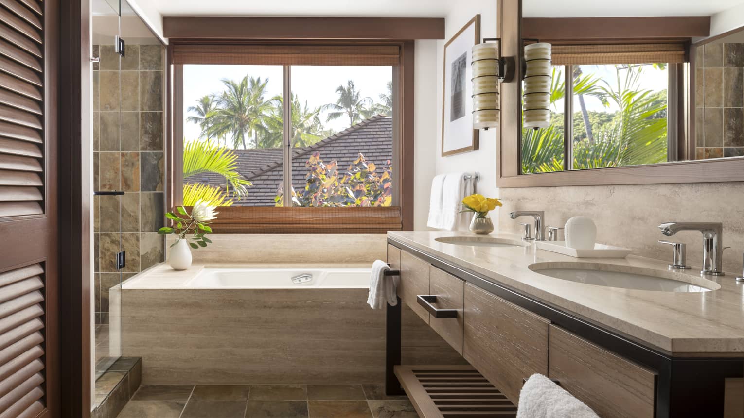Bathroom with tub underneath large window, earth-tone tile floors, double vanity