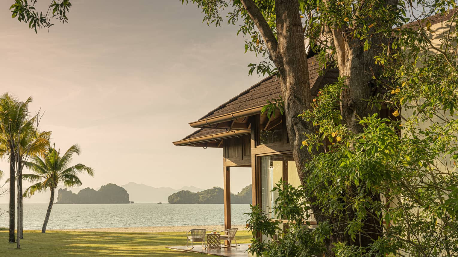 Green lawn with covered terrace and palm trees, leading to a beach in Langkawi