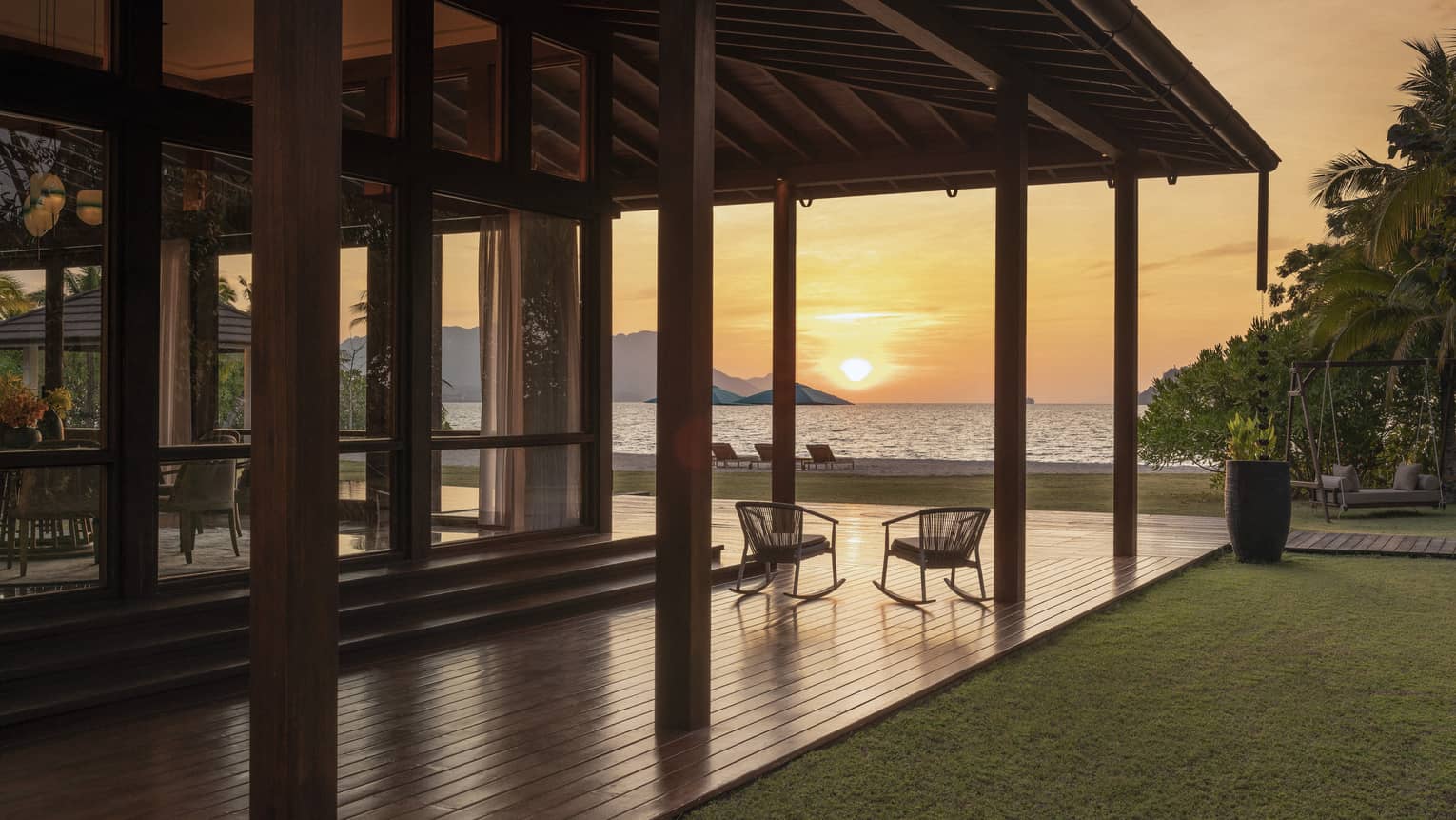 Wrap-around wooden terrace of private villa, looking out to beach at sunset