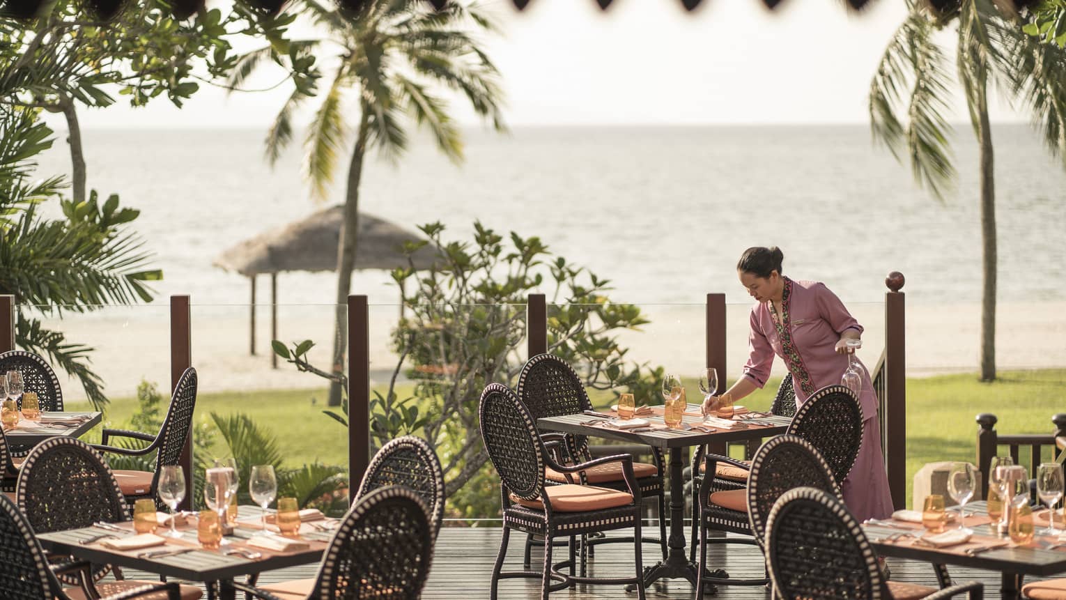 A server at Ikan Ikan sets a table on the outdoor terrace overlooking the beach