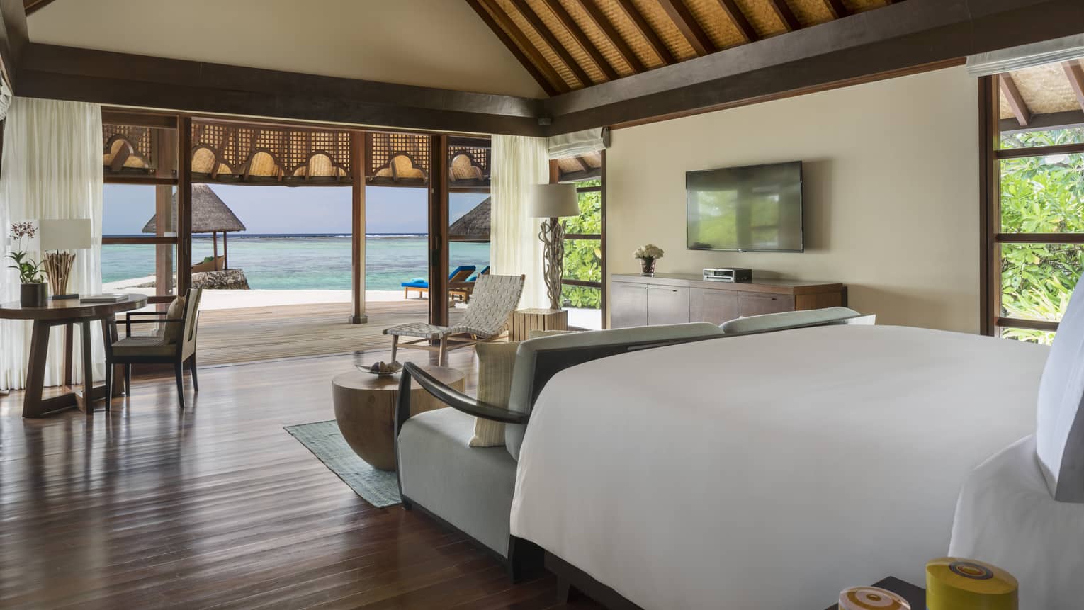 Oceanside bungalow room with wooden furniture and white bedding opening up to ocean