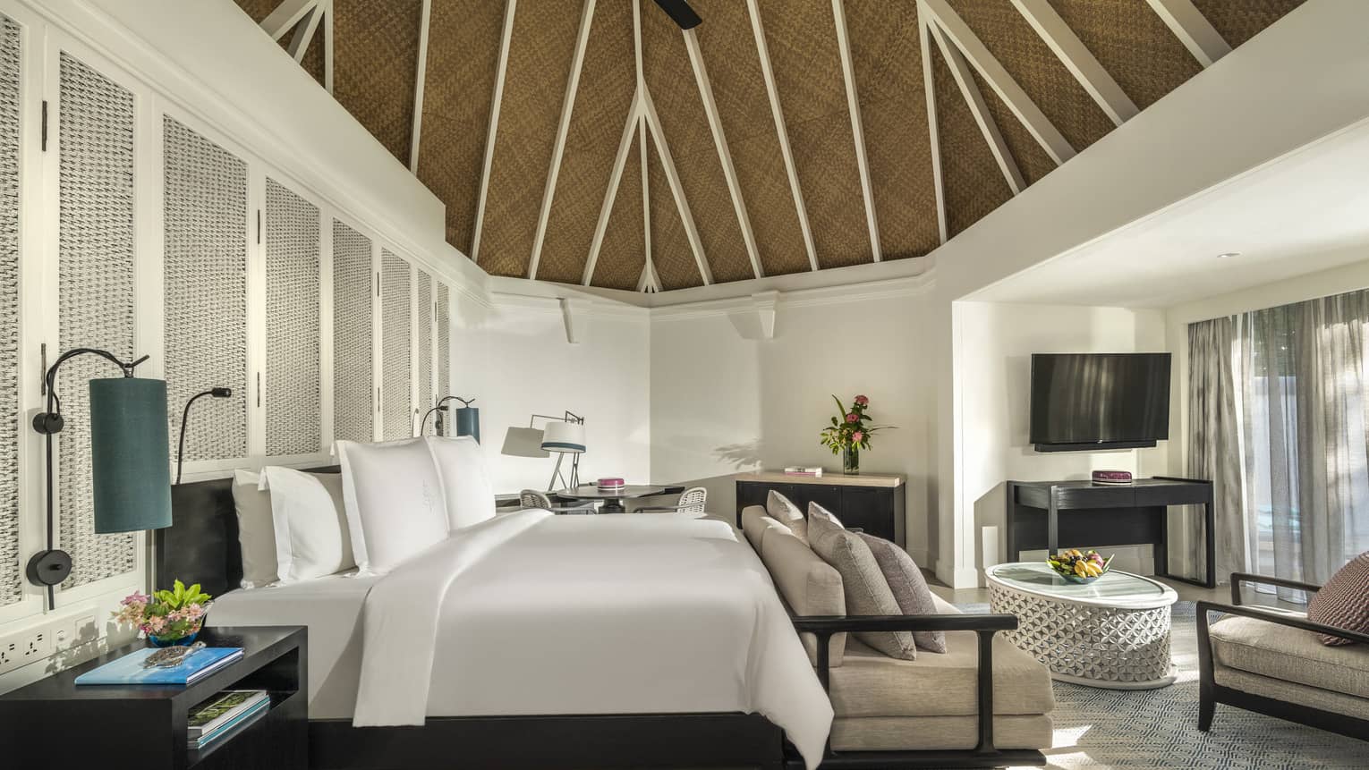Beach pavilion bedroom with a king-size bed, vaulted thatched ceiling, cozy seating area and a flatscreen TV