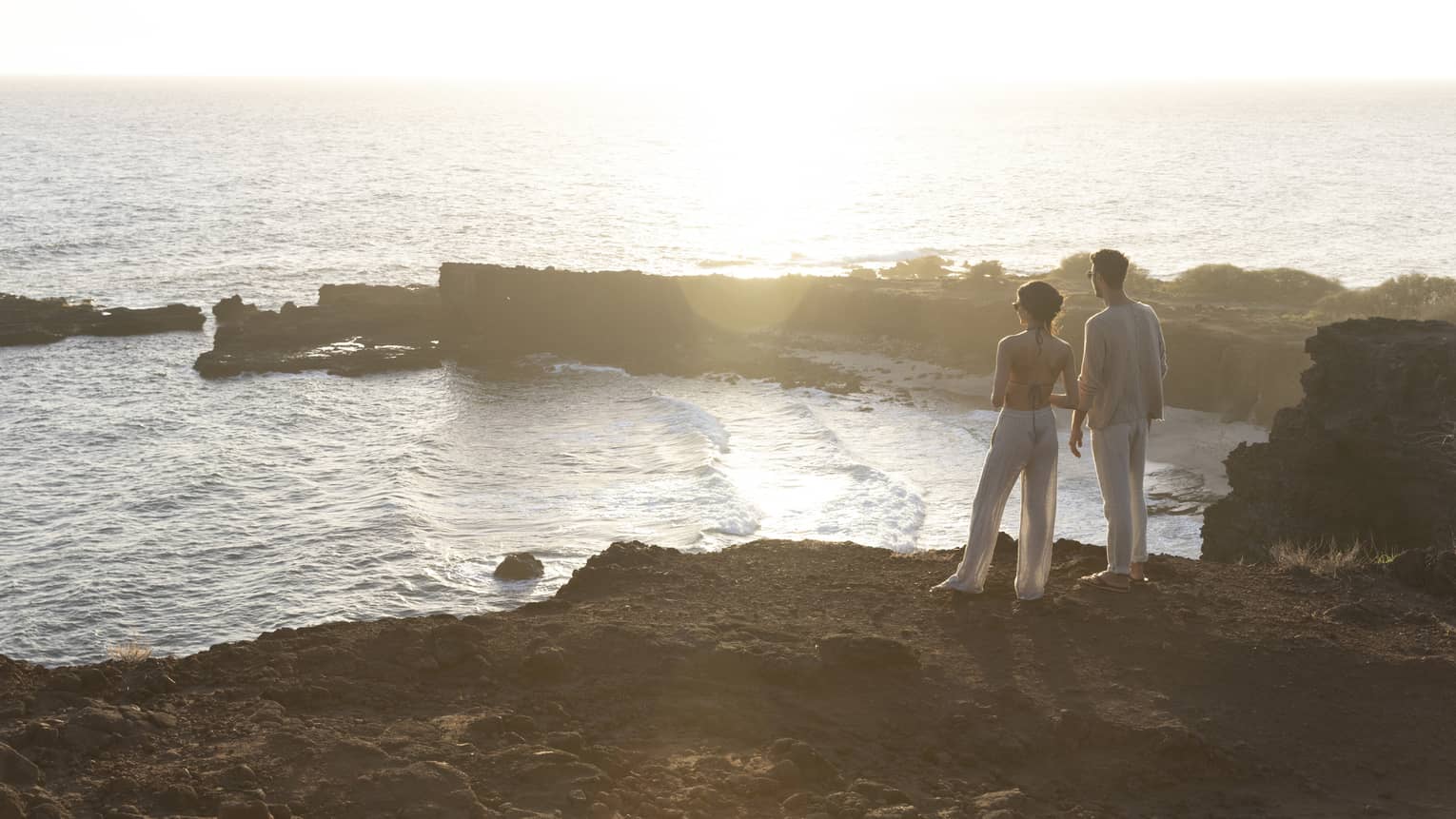 A man and woman stand on top of a cliff overlooking bay in Hawaii