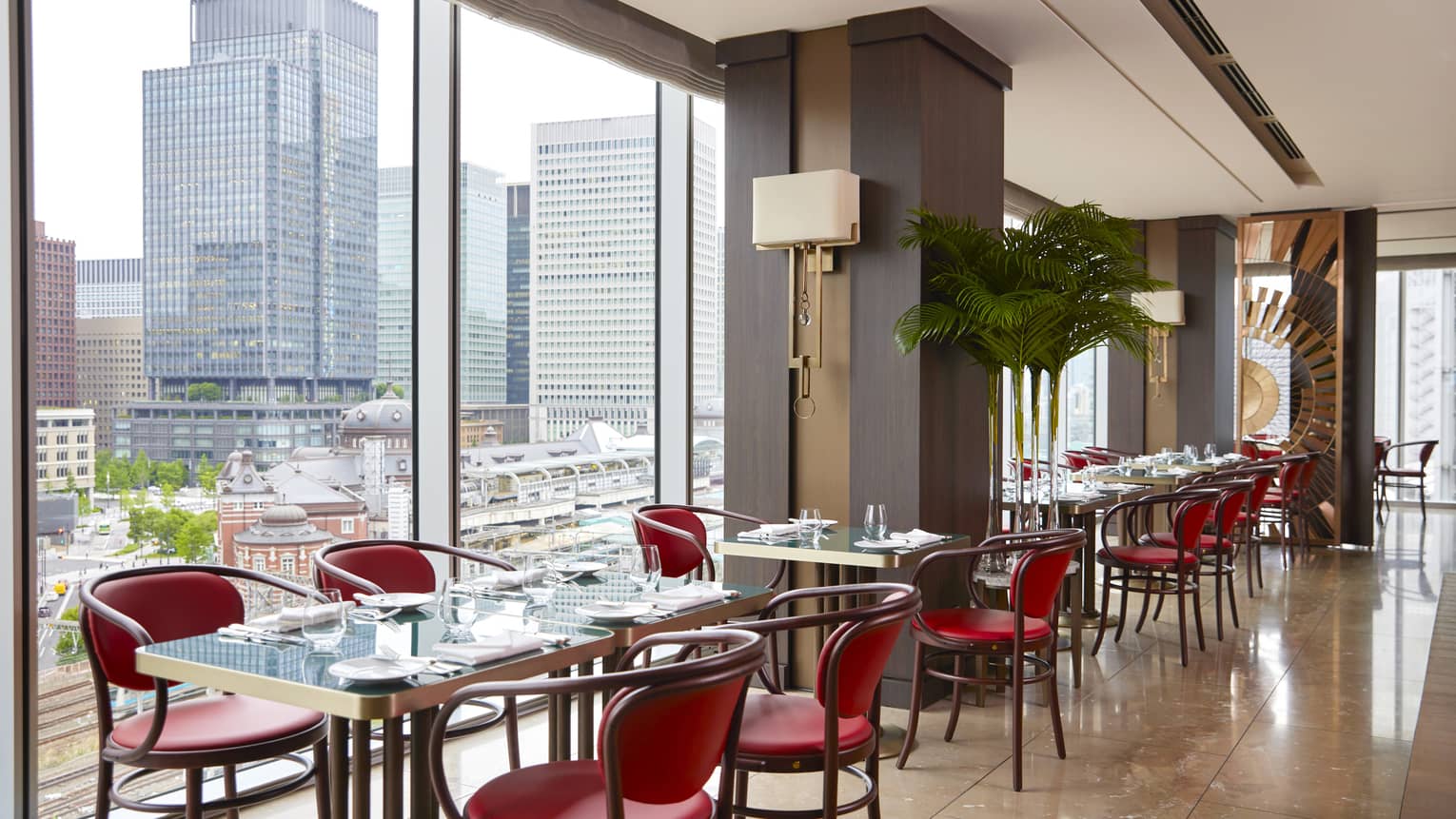 Row of four tables with four chairs each at Maison Marunouchi, floor-to-ceiling windows with views of downtown Tokyo
