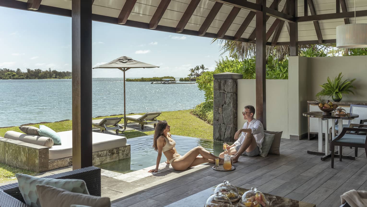 Man and woman sit on wooden terrace next to small pool, sea view