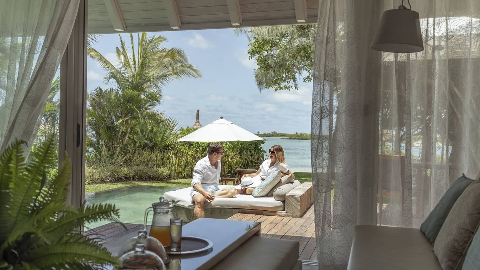 Man and woman outside on wooden terrace with pool and beach view