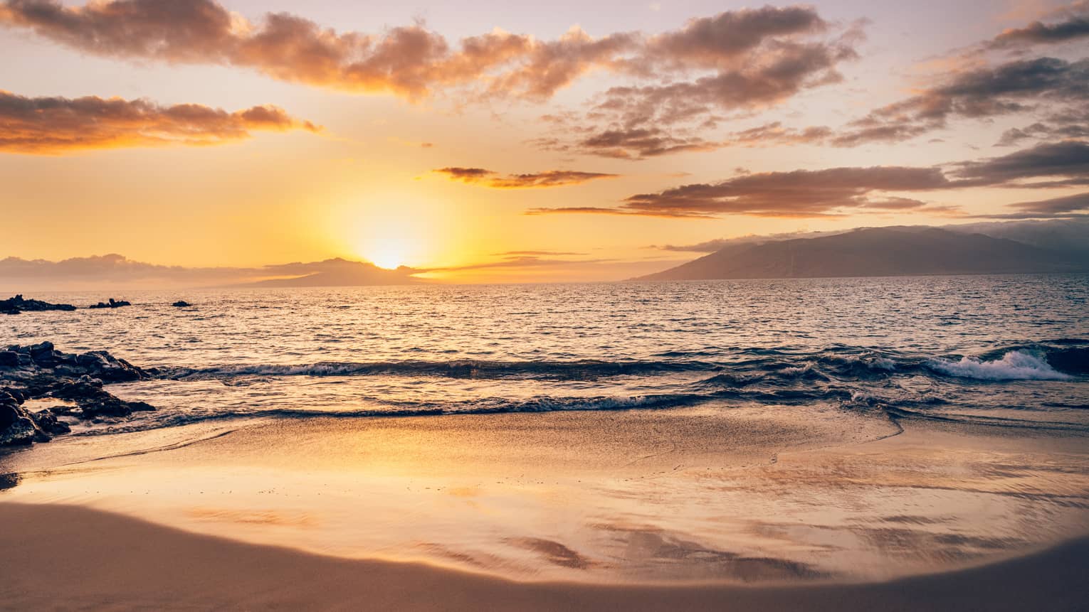Serene beach at sunset with soft waves, golden light reflecting on the sand and clouds over the ocean horizon