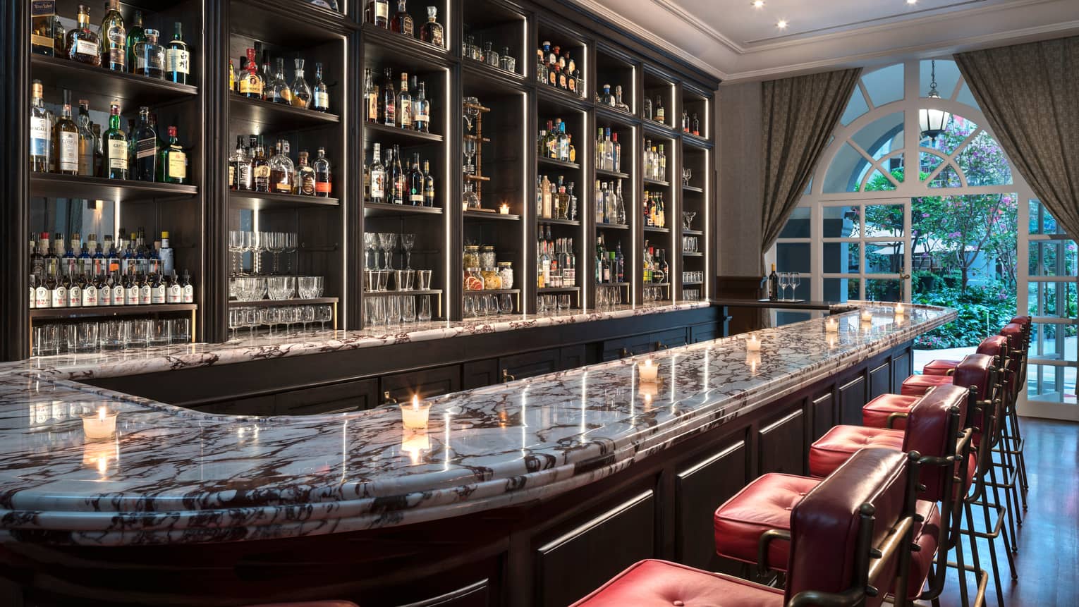Fifty Mils curved marble bar top with candles, liquor on shelves, arched windows