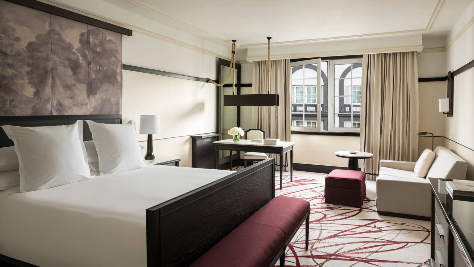 Deluxe Room bed, padded printed headboard, purple bench at foot, sofa and desk by window